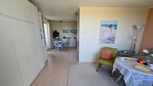 Ein geräumiger Wohnbereich mit Esstisch für zwei Personen, einem grünen Sessel und einem Gemälde mit Strandmotiv.