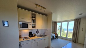 Eine kompakte Küche mit Mikrowelle, Kaffeemaschine und Spüle. Es gibt einen Essbereich mit Tisch und Stühlen sowie einen Meerblick durch große Fenster.