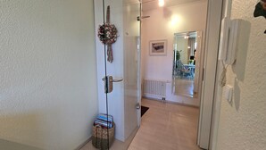 Ein Flur mit Glastür, einem Korbwäscher voller Bücher, einer Heizung, einem Spiegel und einem Telefon.
