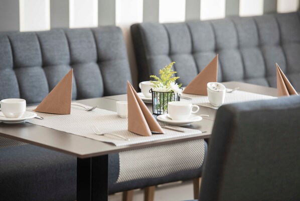 A dining area with grey upholstered booths, white table settings, and a small plant centerpiece.