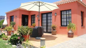 Uma casa com um espaço de pátio, mobiliário de exterior, vasos de plantas e um grande guarda-sol.
