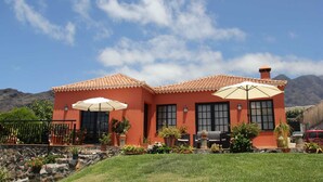 Uma casa de dois andares com fachada vermelha, telhado em telhas e um alpendre com guarda-sóis.