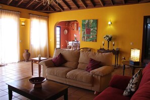 Ein Wohnzimmer mit beiger Couch, einem roten Sessel, einem Holztisch und einem Essbereich mit Tisch und Stühlen.