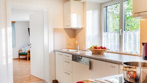 Una cocina con armarios blancos, un lavavajillas Bosch, una ventana con vistas a follaje y una encimera con una cesta de fruta.