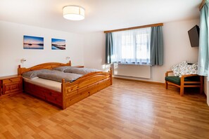 Ein Schlafzimmer mit einem hölzernen Bett, einem Nachttisch, einem Sessel, einem Fenster mit Vorhängen und zwei Wandbildern.