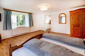 Ein Schlafzimmer mit einem hölzernen Bett, einem Fenster mit Vorhängen, einem Spiegel und einem Holzschrank.