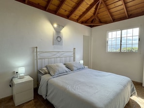 Une chambre à coucher comprenant un lit, des tables de chevet, une lampe fixée au mur, une fenêtre et une vue sur l’extérieur.