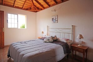 Une chambre à coucher comprenant un lit, deux tables de chevet, une fenêtre et un plafond avec des poutres en bois.