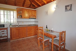 Una cocina con armarios de madera, salpicadero de azulejos, una mesa de comedor con sillas y una ventana con persianas.
