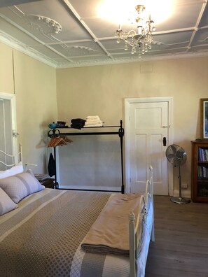Une chambre à coucher comprenant un lit, une table de chevet, une armoire, un radiateur, un ventilateur et une porte.