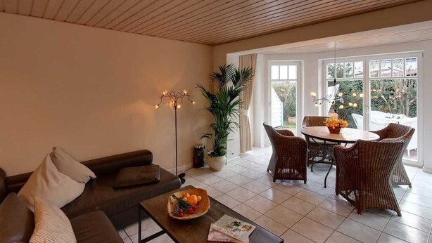 A modern living room with a sofa, coffee table, and dining area with wicker chairs. - Fewo 1 - Ferienwohnung - Schmidt (Kühlungsborn)
