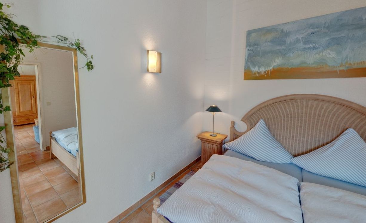 A bedroom with a bed, a nightstand, a lamp, a mirror, and a painting on the wall.
