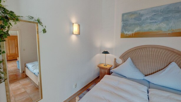 A bedroom with a bed, a nightstand, a lamp, a mirror, and a painting on the wall. - Apartment 5 - Holiday apartment - Schmidt (Kühlungsborn)