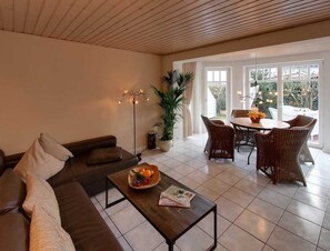Una sala de estar moderna con un sofá, una mesa de centro y una zona de comedor con sillas de mimbre.