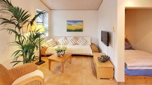 Ein gemütliches Wohnzimmer mit einer Sofagarnitur, einem Couchtisch, einem Fernseher und einer großen Pflanze.