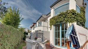 Ein Wohnhaus mit einer Terrasse, die Korbmöbel und eine Glastür zu einem überdachten Außenbereich aufweist.