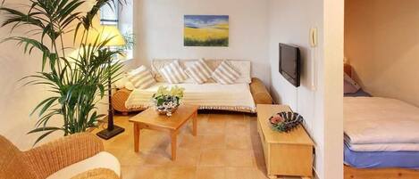Una sala de estar acogedora con un conjunto de sofá, una mesa de centro, un televisor y una planta grande.