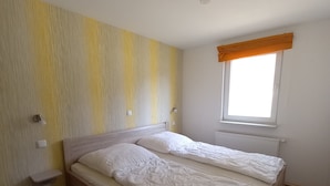 Een slaapkamer met een houten bed, een nachtkastje, een wandlamp, een raam met gordijn en een radiator.
