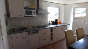 Een keuken met witte kastjes, een magnetron, een spoelbak en een raam.