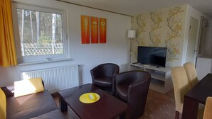 Een woonkamer met een bank, fauteuils, een salontafel, een televisie en een open haard.