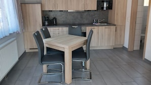 Una cucina moderna con mobili in legno chiaro, un piano di lavoro nero e un lavello in acciaio inossidabile. Si nota un tavolo da pranzo con quattro sedie.