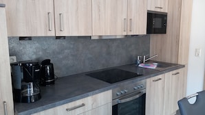 Una cucina moderna con mobili chiari in legno, un piano di lavoro nero, un forno integrato e un forno a microonde.