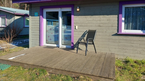 Una baita con una veranda coperta, una porta scorrevole in vetro e una sedia.