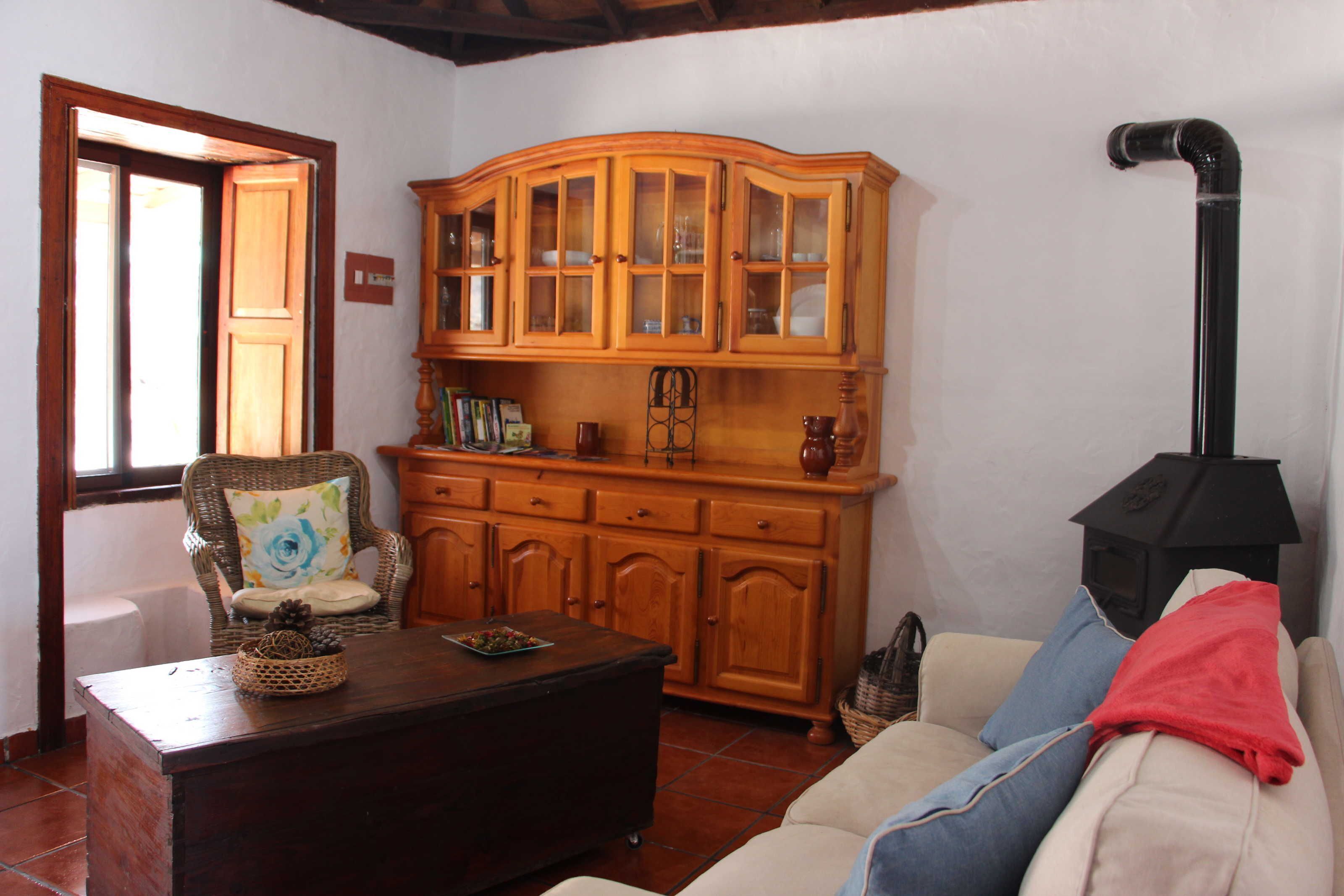 A living room with a wooden cabinet, a wicker chair, a sofa, and a fireplace.