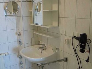 Une salle de bain avec un lavabo blanc, un miroir et un sèche-cheveux posé sur un support.
