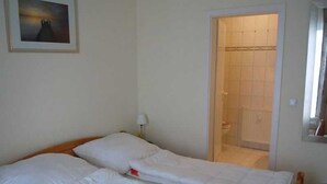 Une chambre avec deux lits, un tableau encadré au mur et une porte de salle de bain visible.