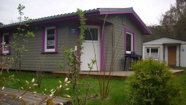 A small, single-story cabin with a purple trim and a number '5' sign on the door.