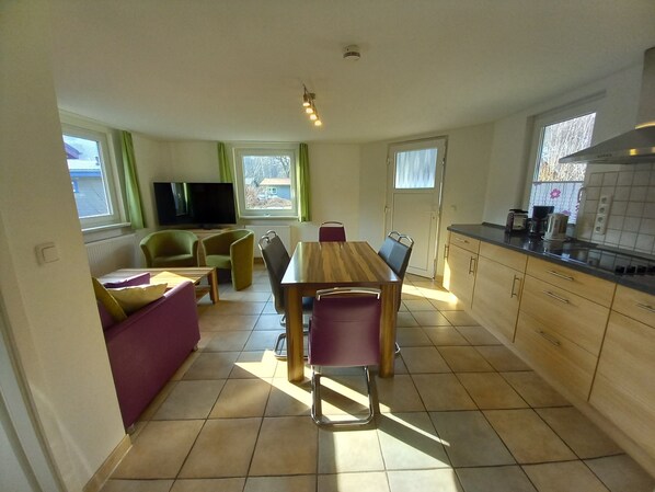 Un espacio habitable compacto con una mesa de comedor, sillas, un sofá, un televisor y una cocina con armarios y ventana.