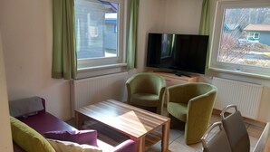 A living room with a sofa, two armchairs, a coffee table, a flat-screen TV, and windows with curtains.