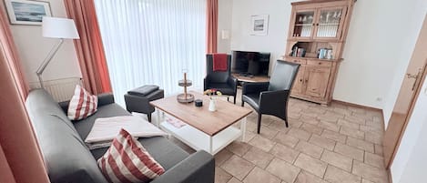 A modern living room with a sofa, a coffee table, and a TV. There is a wooden cabinet and a lamp.
