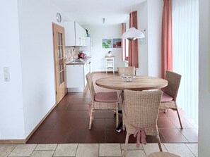 A modern kitchen with white cabinets, a round dining table with wicker chairs, and a view of the living area.