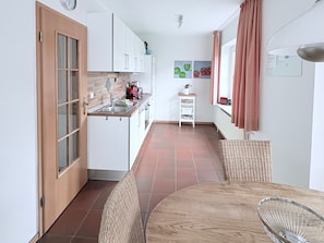 Une cuisine de taille réduite avec une porte en bois, des placards blancs, un évier et une petite table avec des chaises.