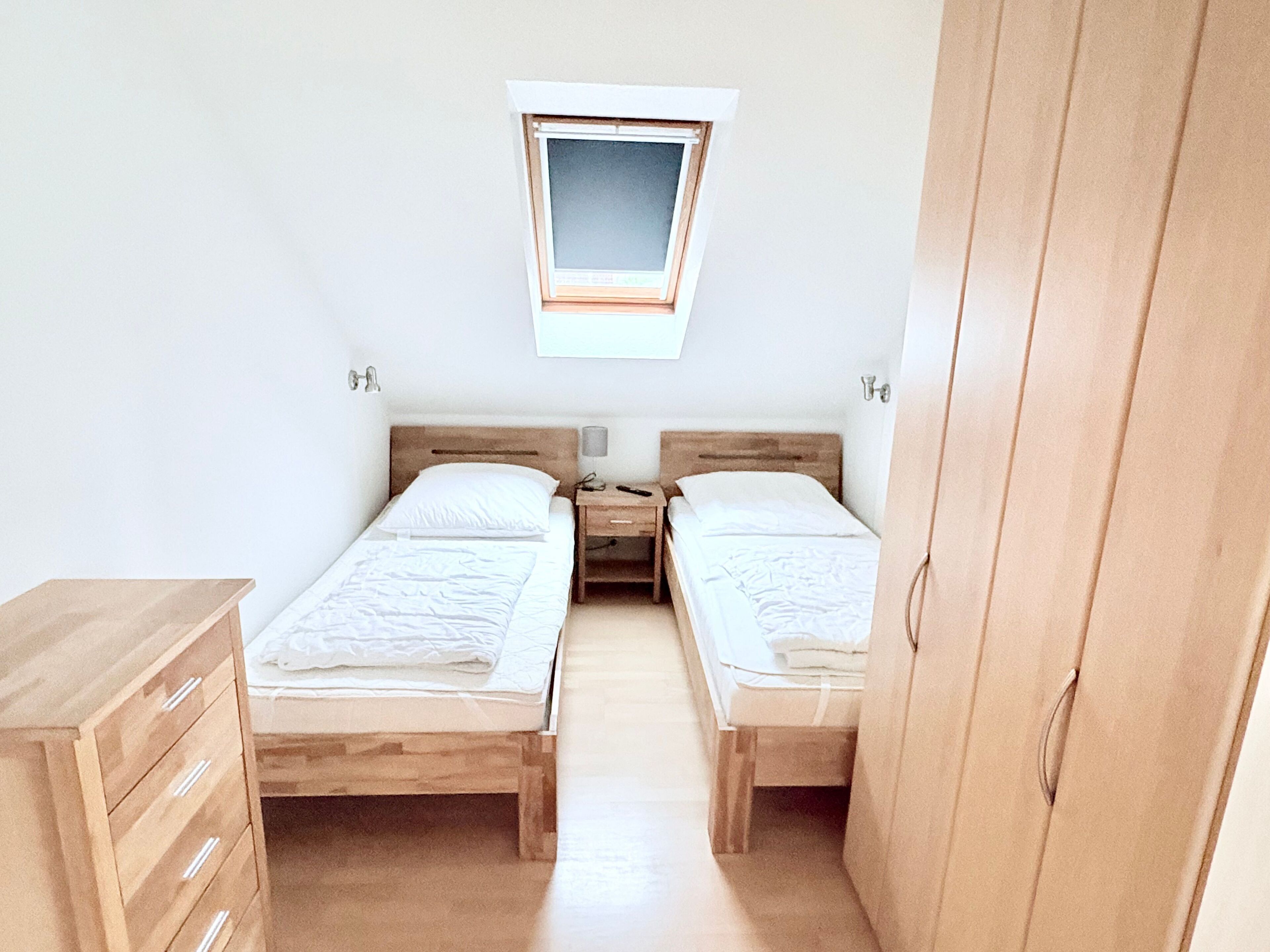 Una habitación con dos camas individuales, un aparador de madera, una mesita de noche y un ventanal.