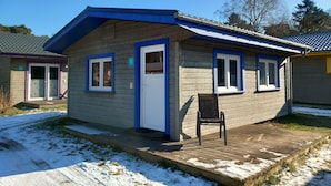 A small wooden cabin with a blue roof and white trim, a porch with a chair, and a number '9' sign.