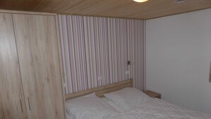 Una camera da letto con un armadio in legno, una testiera a righe e un letto bianco.