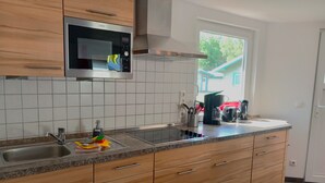 Una cocina moderna con armarios de madera, un microondas de acero inoxidable, un lavamanos y una ventana con vista a una casa.