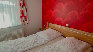Un dormitorio con cama, radiador, ventana con cortinas y pared con diseño floral rojo.