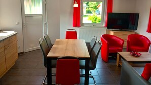 Un espacio habitable compacto con zona de comedor, televisor y ventana con cortinas.