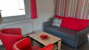 Una sala de estar con un sofá, dos sillas rojas, una mesa de centro de madera y un radiador.