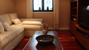 Ein Wohnzimmer mit einer Couch, einem Couchtisch mit einer Schale, einem Fernseher auf einem Holzboden und einem Fenster mit Vorhängen.