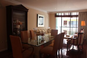 A dining area with a glass table surrounded by chairs, a cabinet with glass doors, and a sofa.
