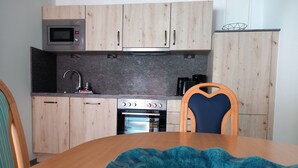 A kitchen with wooden cabinets, a microwave, an oven, and a dining table with a blue placemat. - Ferienwohnung 27, Deutschland (Trassenheide)