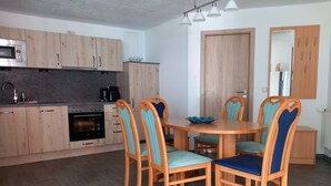 A modern kitchen with wooden cabinets, a built-in oven, and a dining area with a round table and six chairs. - Ferienwohnung 27, Deutschland (Trassenheide)