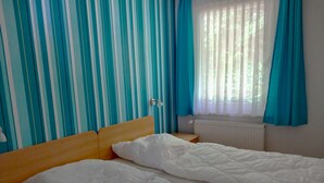 A room with two single beds, striped curtains, a window with curtains, a radiator, and a wooden headboard. - Ferienwohnung 27, Deutschland (Trassenheide)
