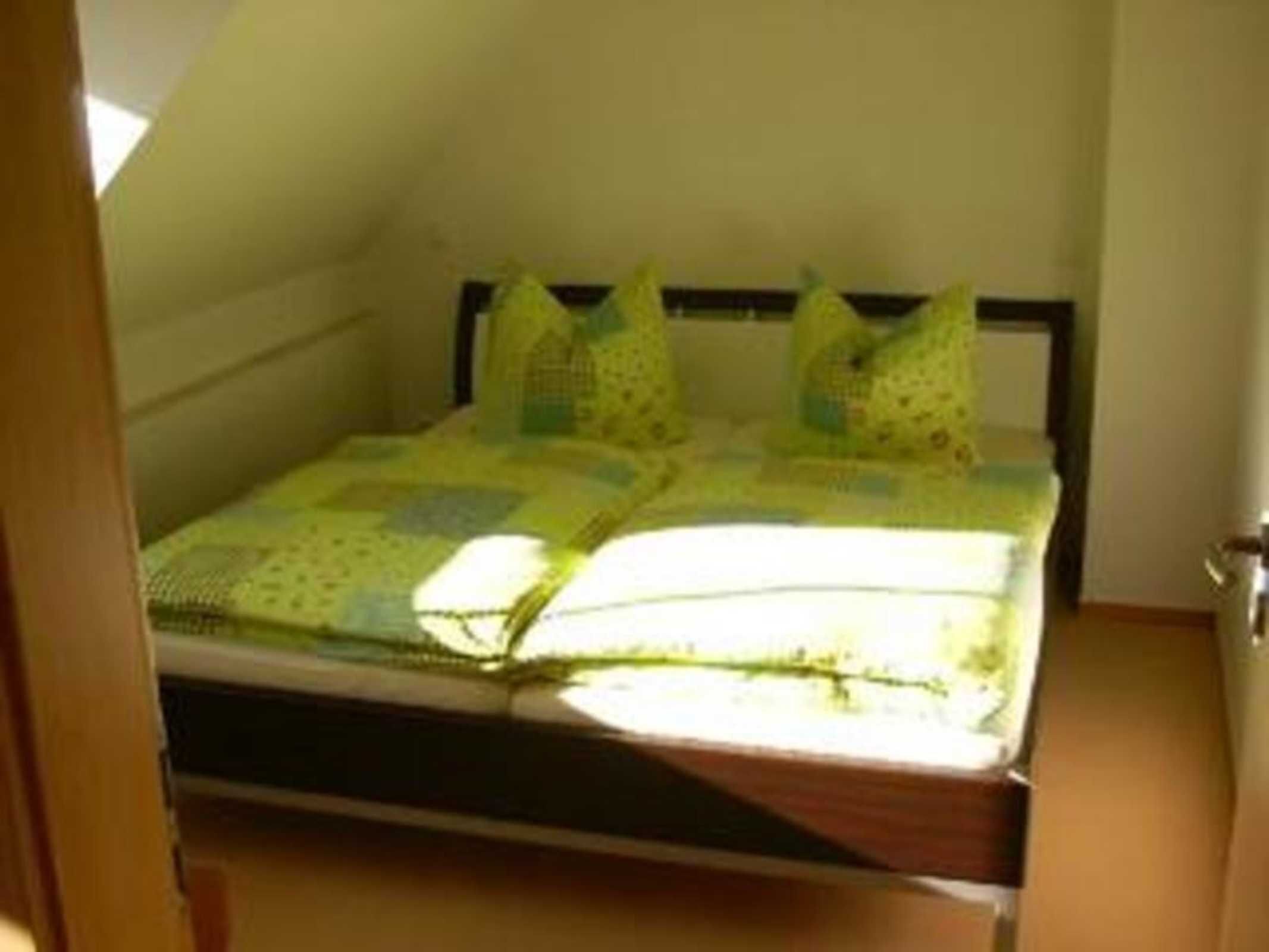Ein kleines Zimmer mit einem einzelnen Bett, schrägem Dach, Holz-Kopfstütze und schlichter Wandgestaltung.