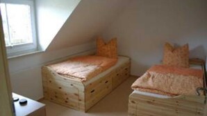 A small, triangular room with two wooden bunk beds, a window, and a small table.